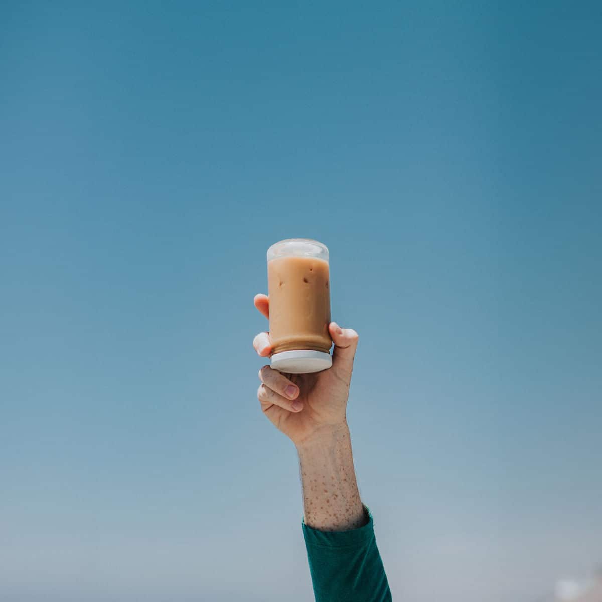 A person holding a glass of THC coffee against a blue sky background.