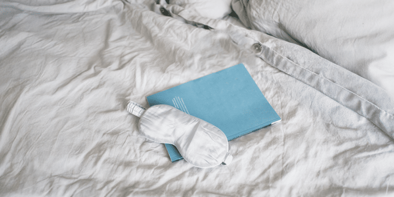 Sleep mask and dream journal sit on a bed’s cozy linens.